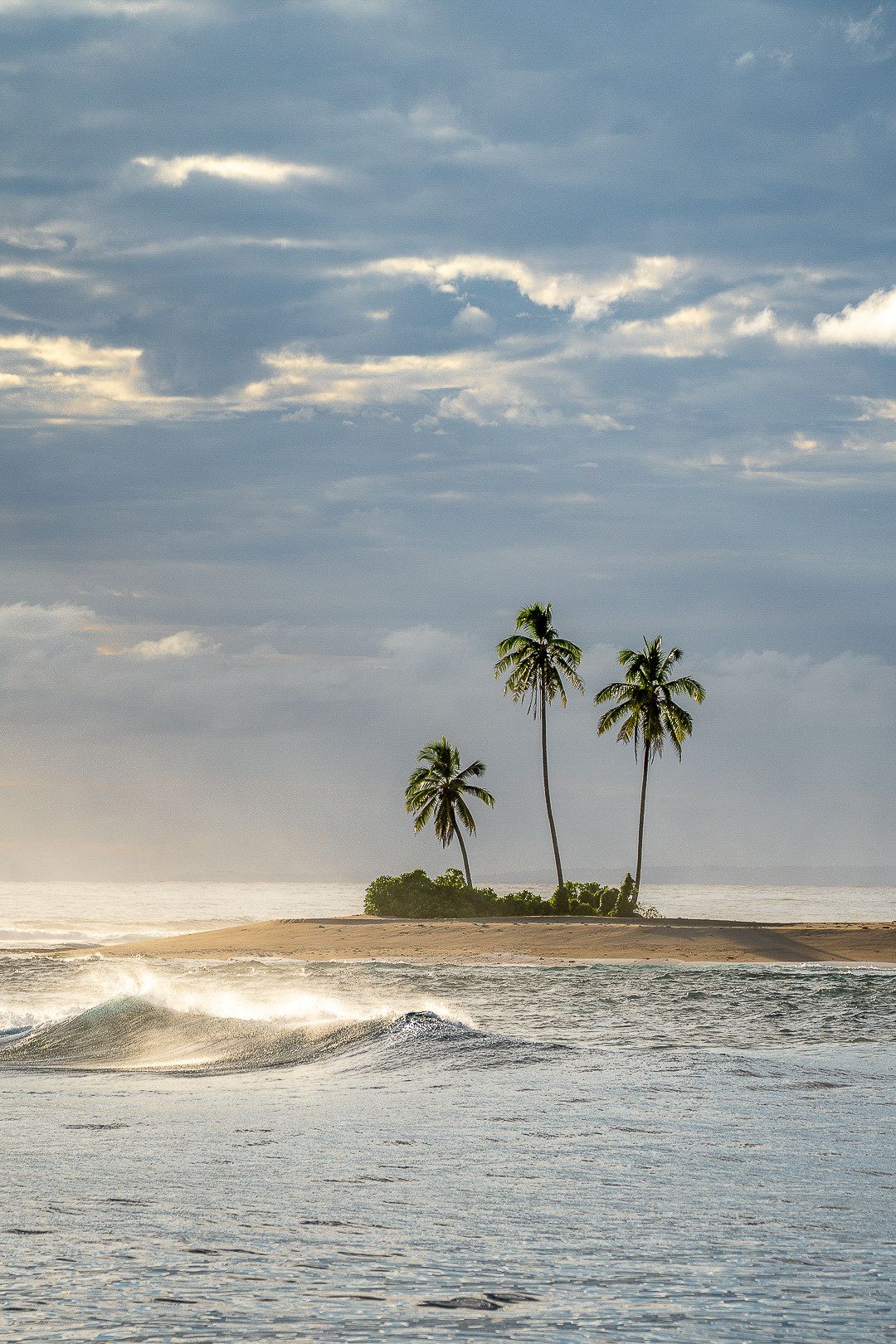 Two palm trees on a tiny sandy islet in the sea.