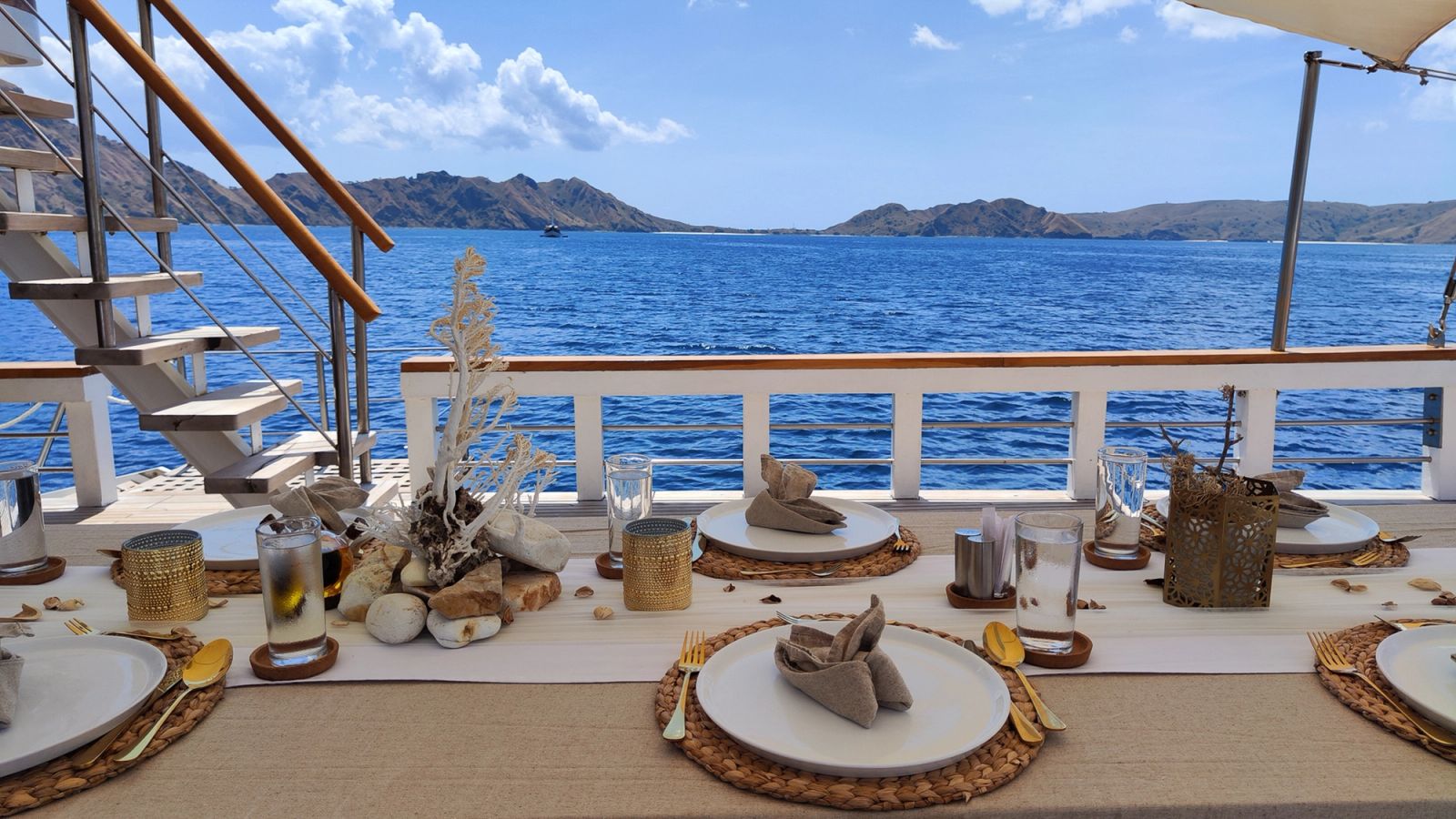 A dining table set for a meal on the deck of Siloina beside the sea.