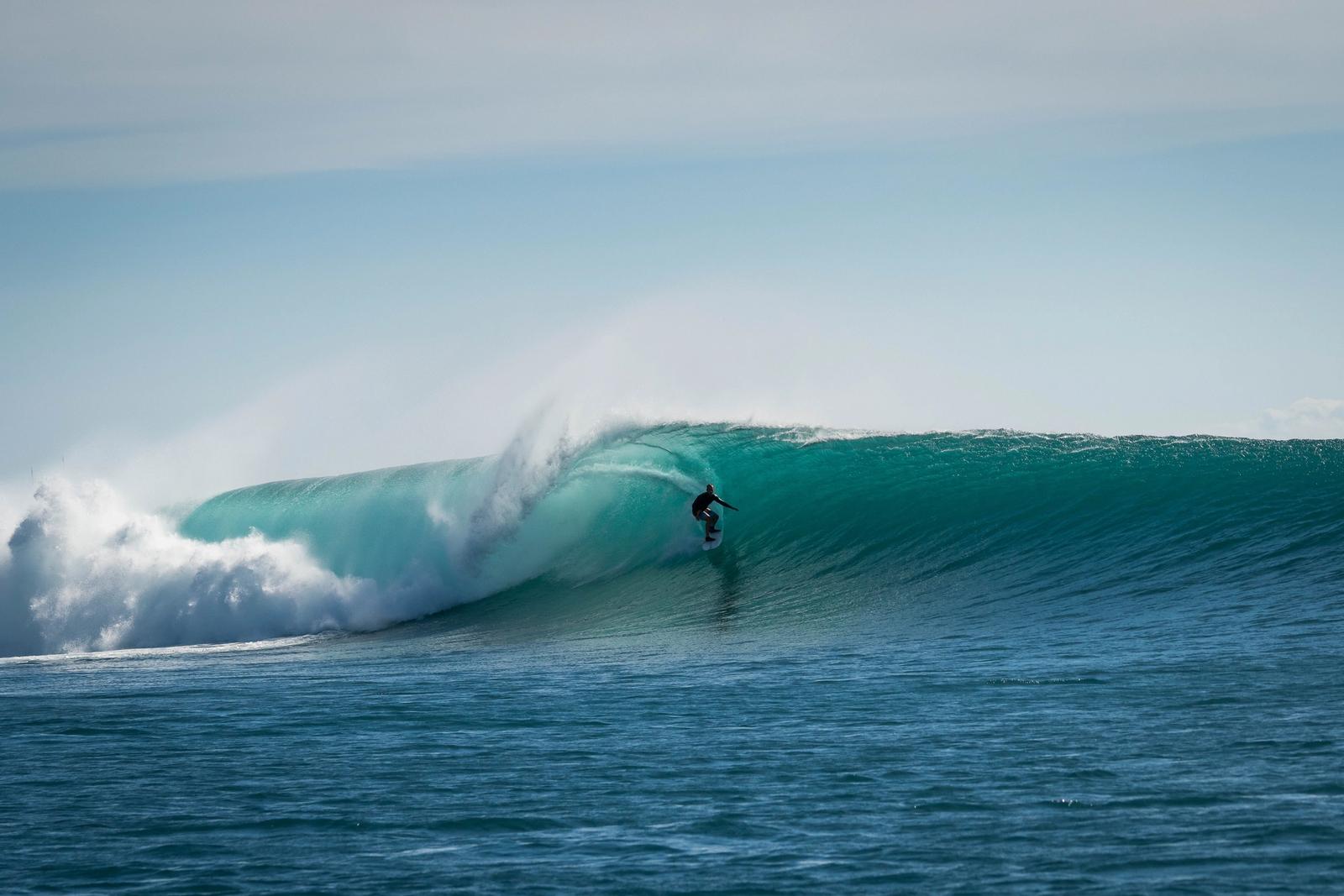 A surfer riding deep inside a turquoise barrel off Sumbawa