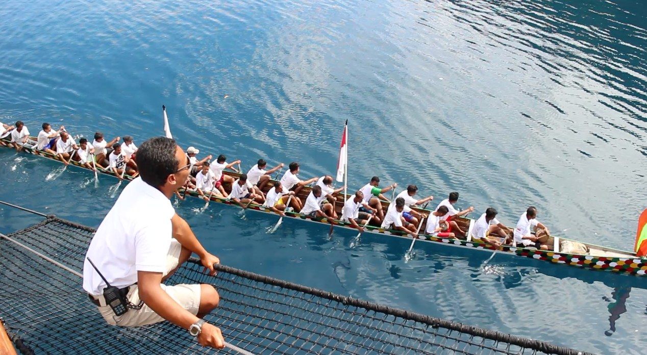 A kora kora crew paddling past a charter yacht in the Banda Islands