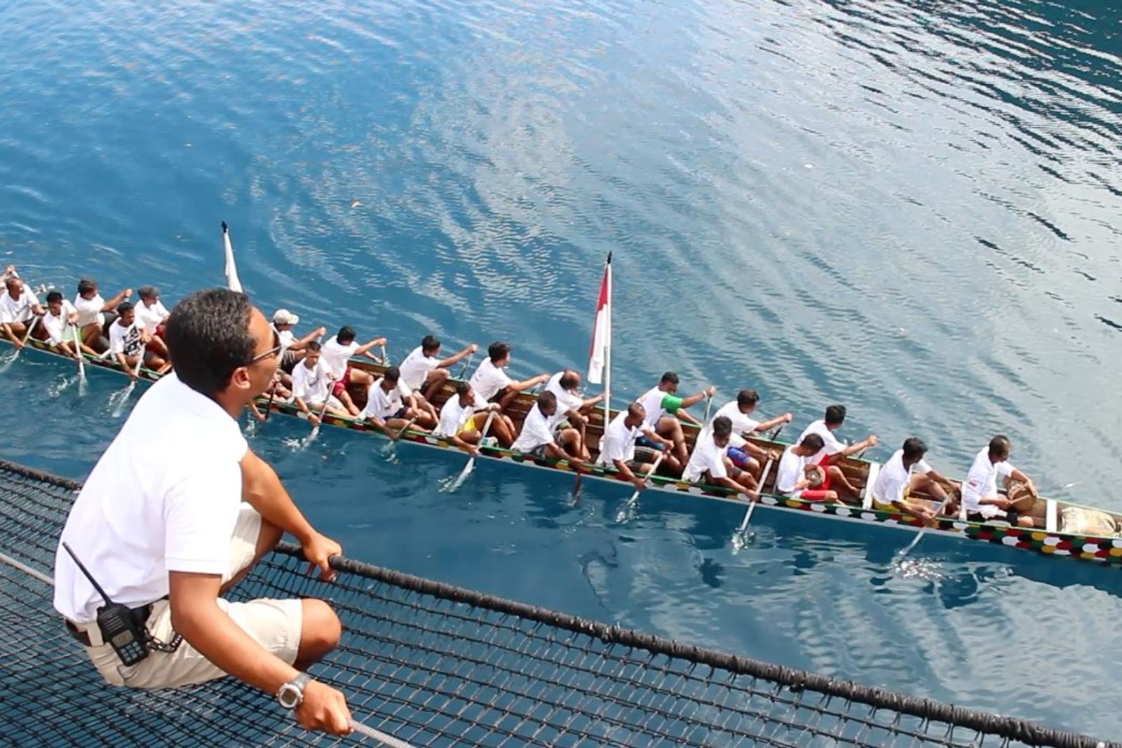 A kora kora crew paddling past a charter yacht in the Banda Islands