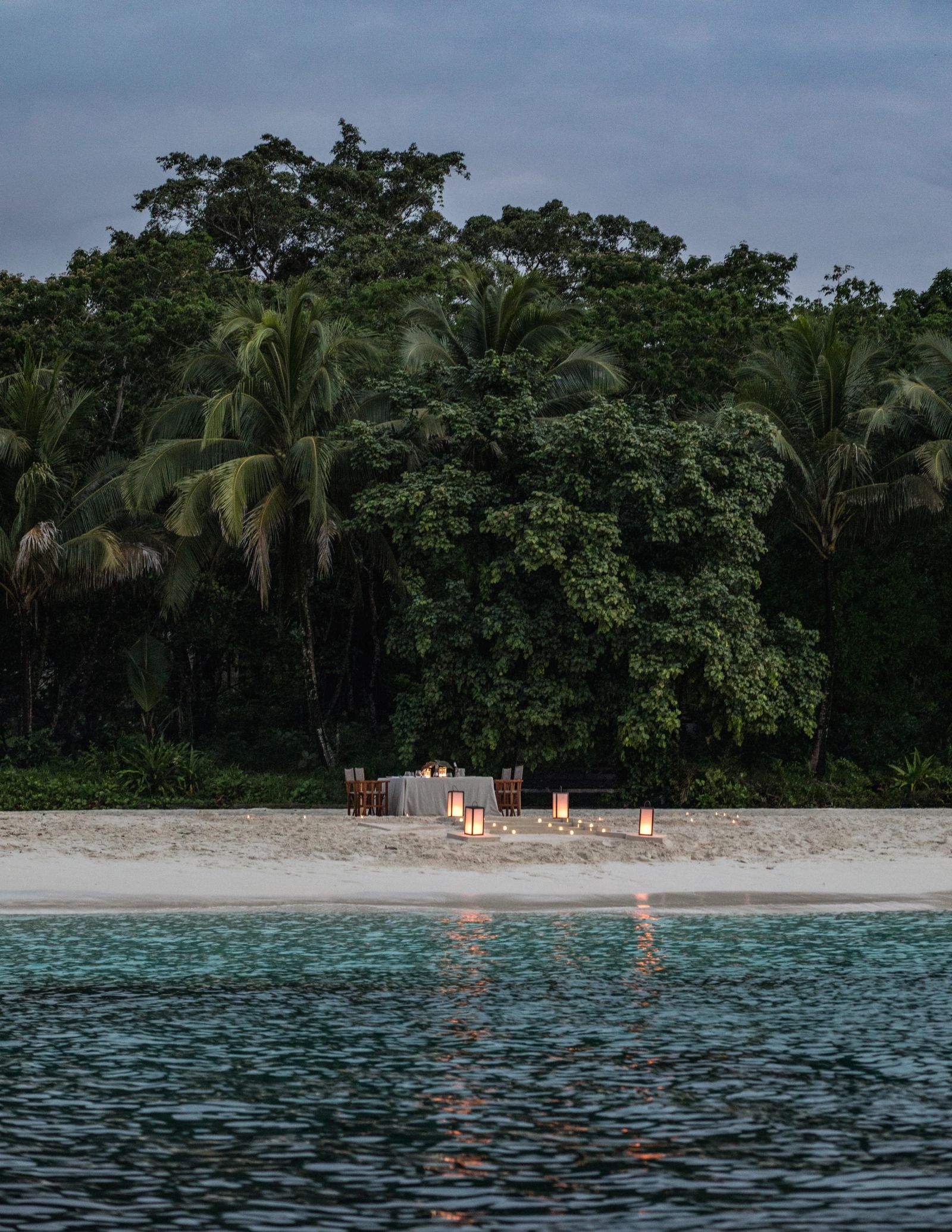 A dinner table set on a beach in front of tall trees