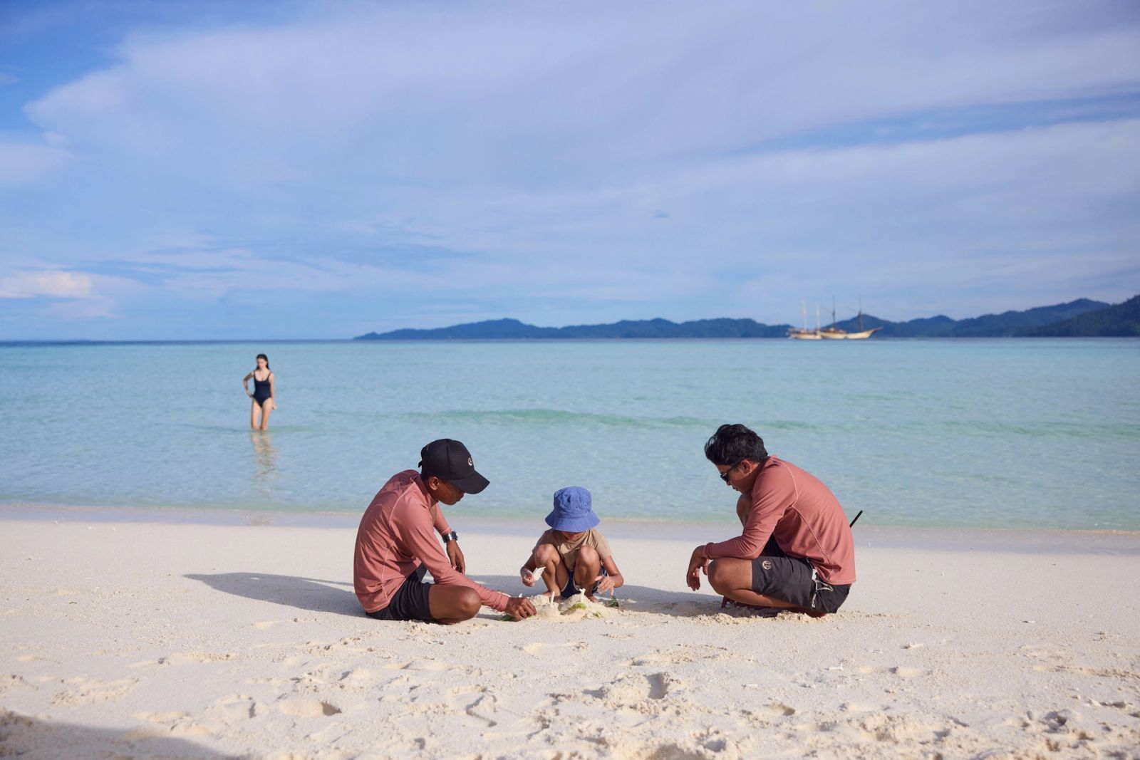 A family on the beach with Silolona at anchor beyond