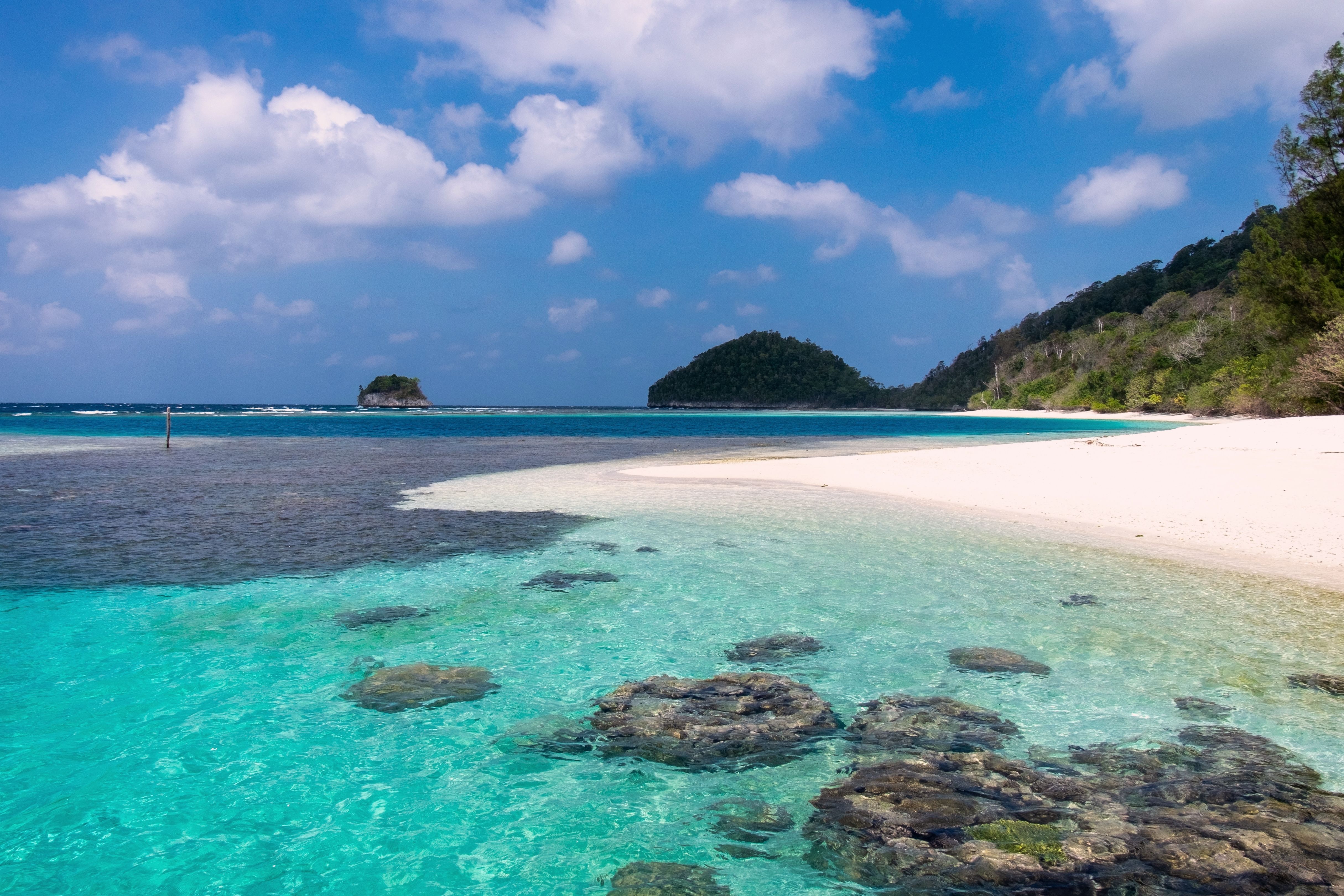 A white beach with dark rocks in clear turquoise shallows