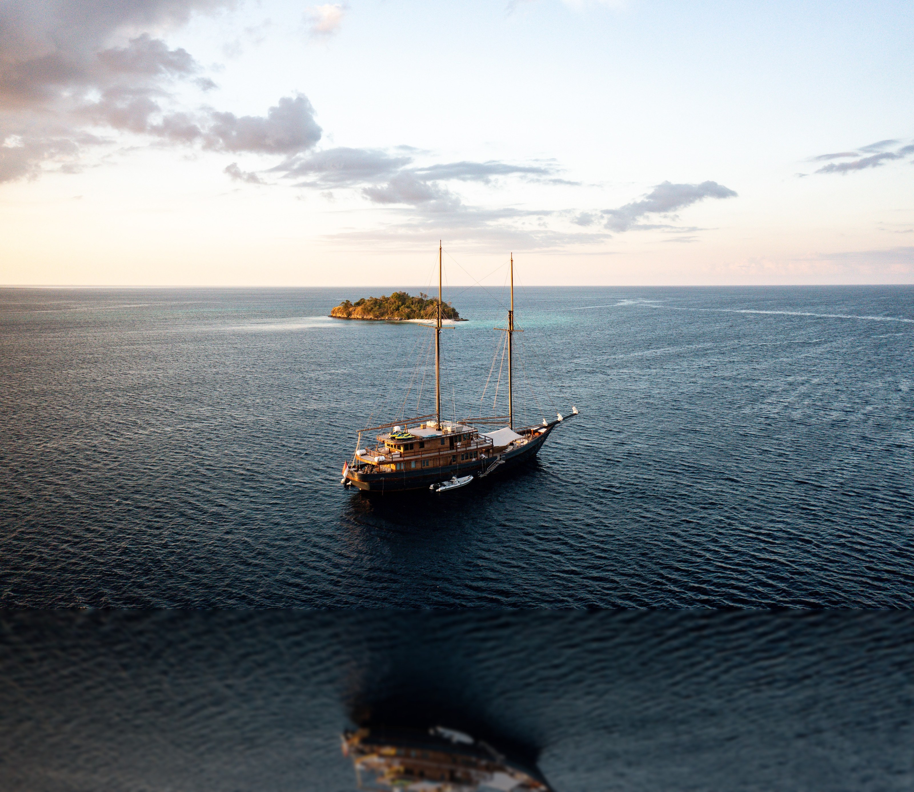 Vela at anchor beneath a burning sunset over the Komodo hills