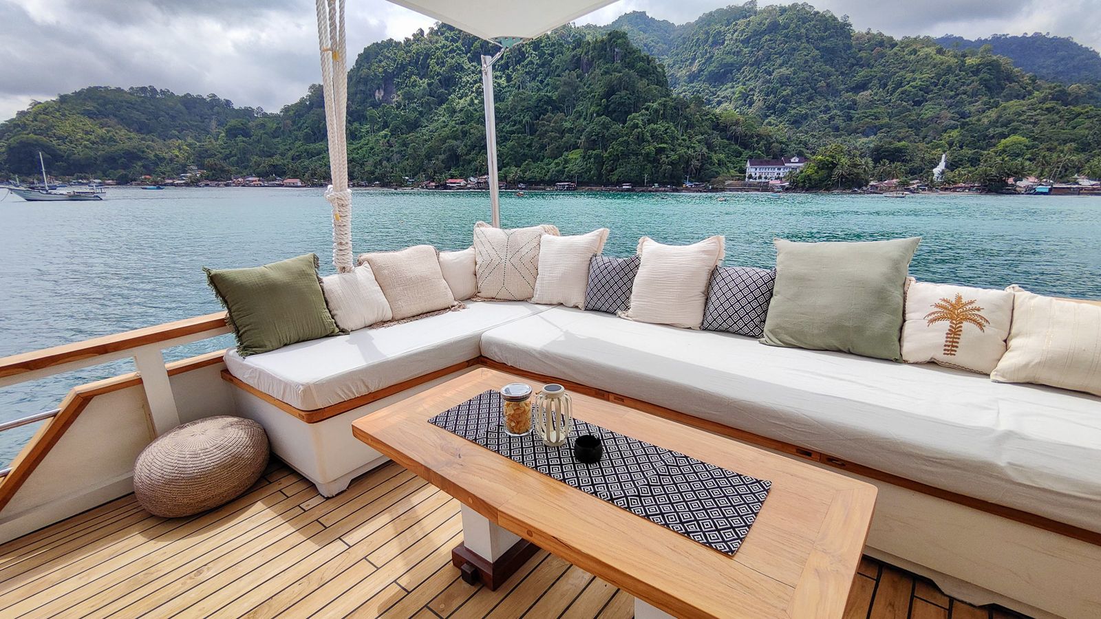 A cushioned corner sofa and low table on the deck of Siloina with green hills beyond.