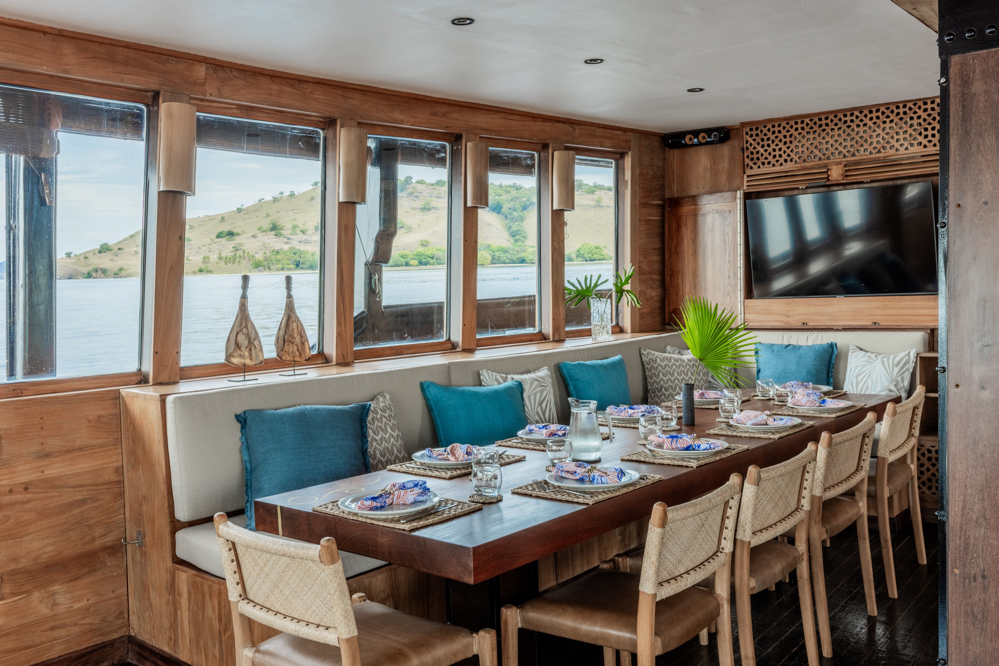 The indoor dining table on El Aleph laid for a meal beside a bench with teal cushions.