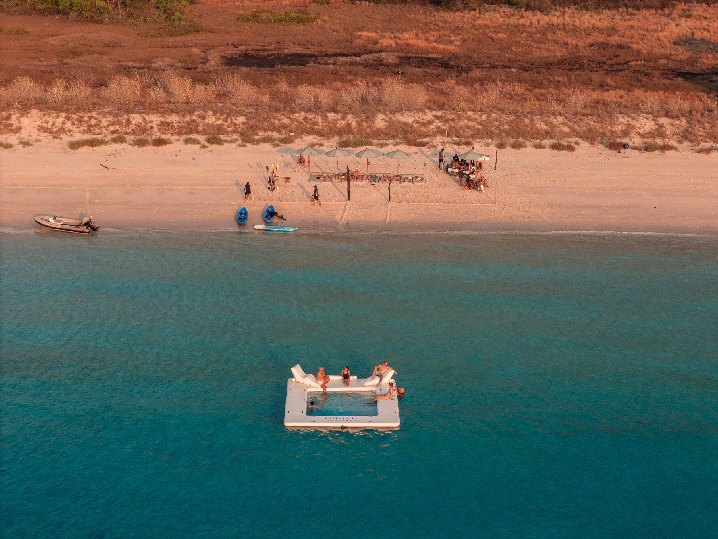 A floating platform in turquoise water off a pink-sand beach, from the air