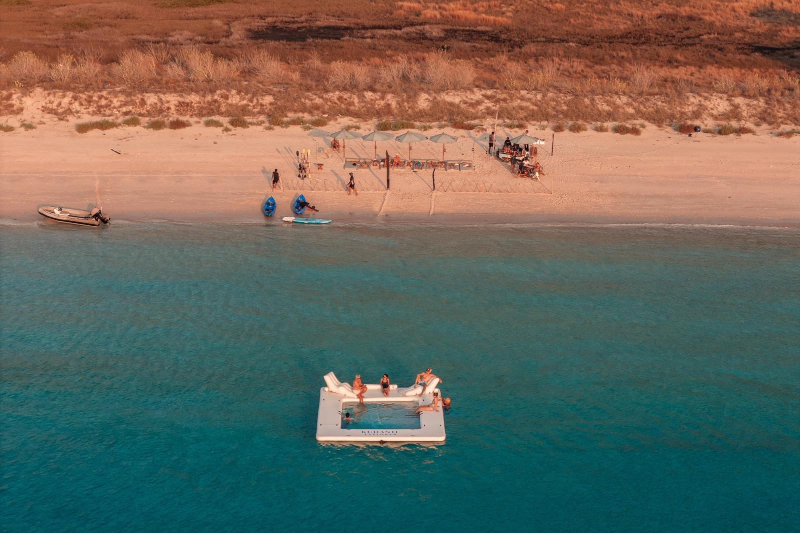 A floating platform in turquoise water off a pink-sand beach, from the air