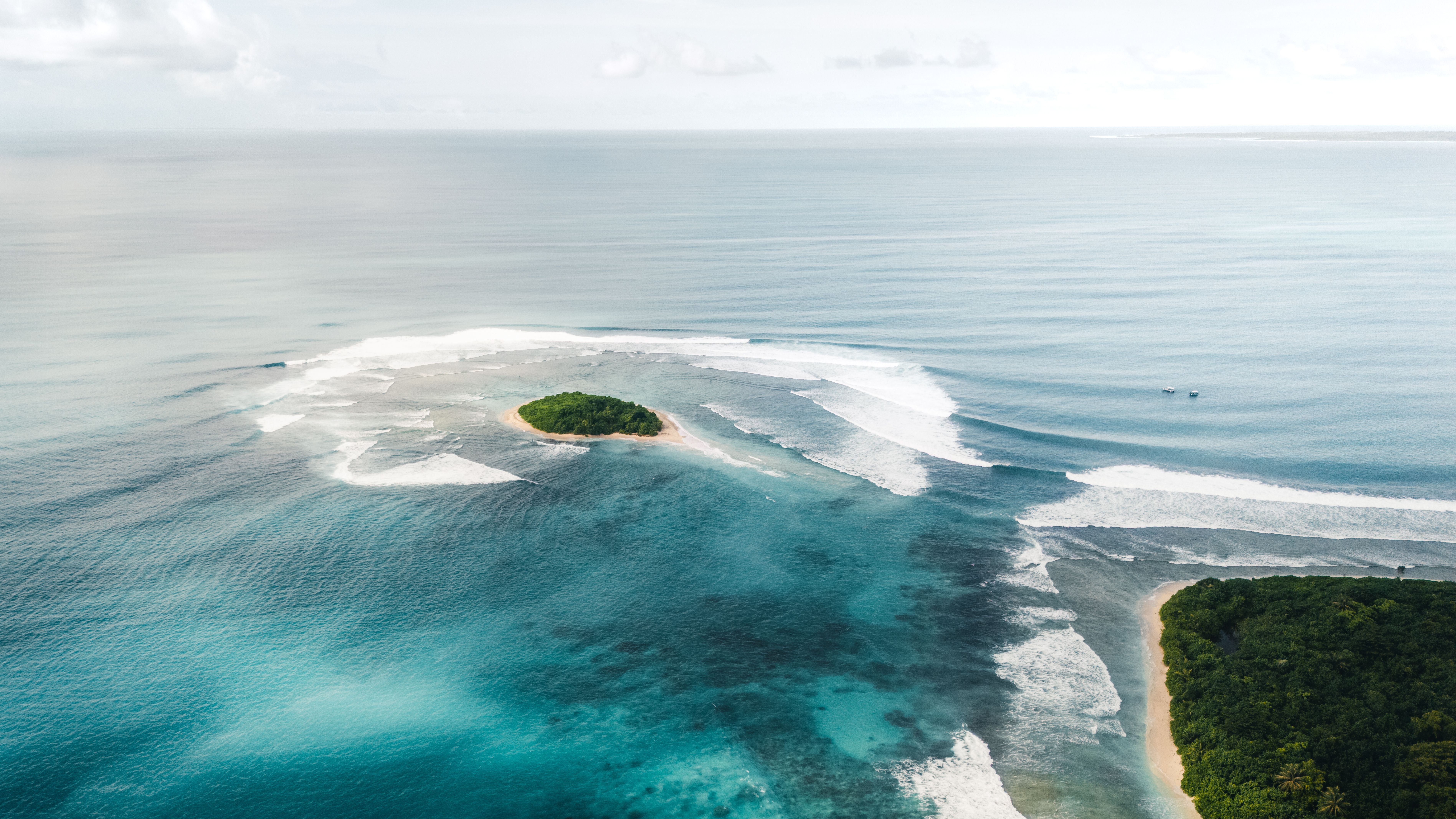 Waves wrapping a small island and its reef pass in the Telo Islands, from the air