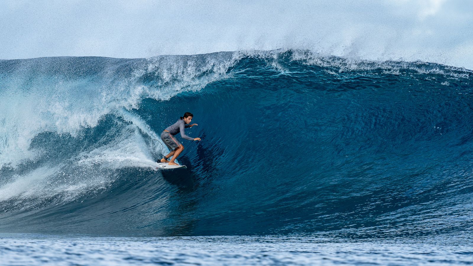 A surfer riding inside a large blue barrel.