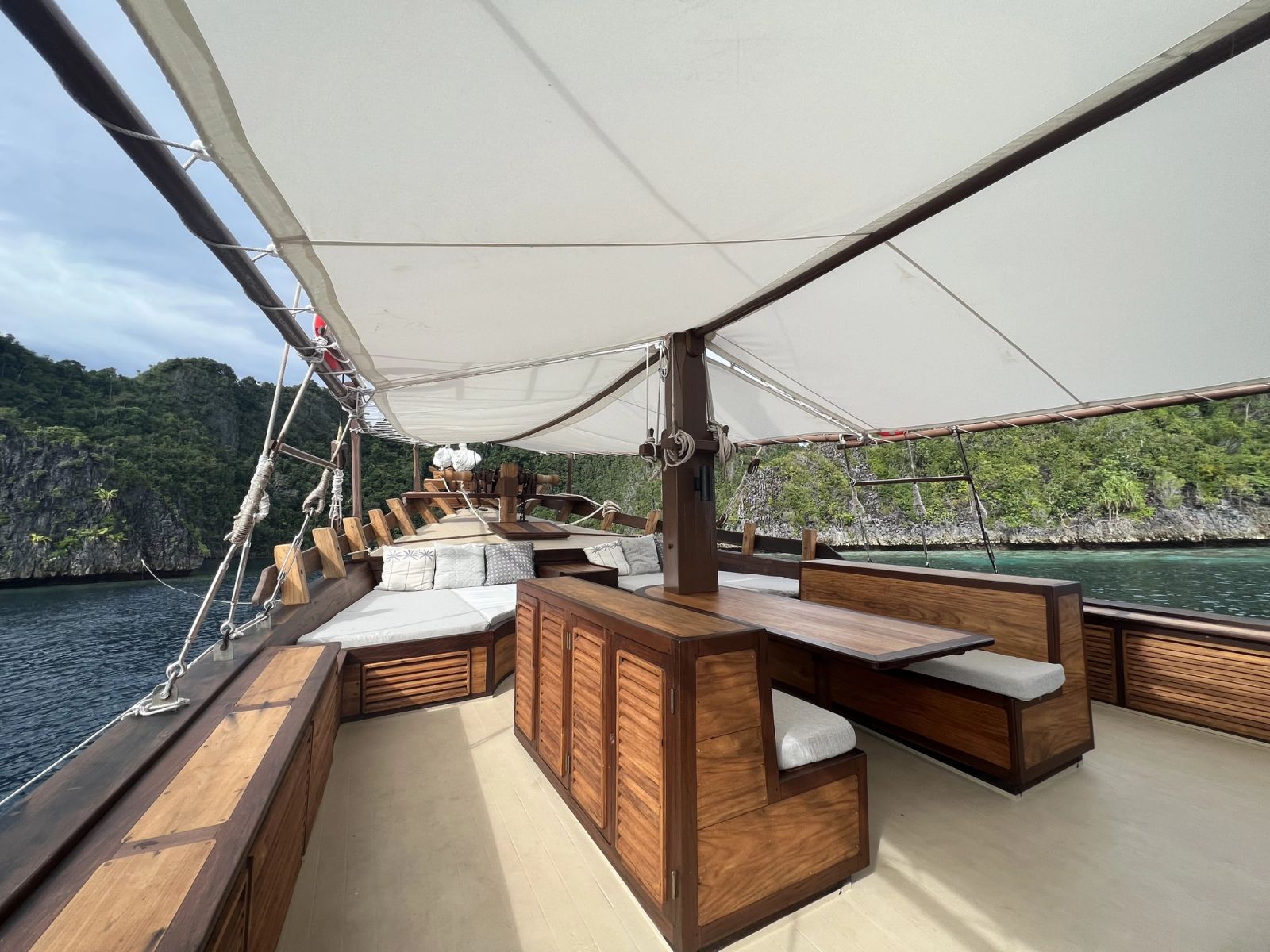 The foredeck on Dewata beneath the awning with a table, benches and a daybed.