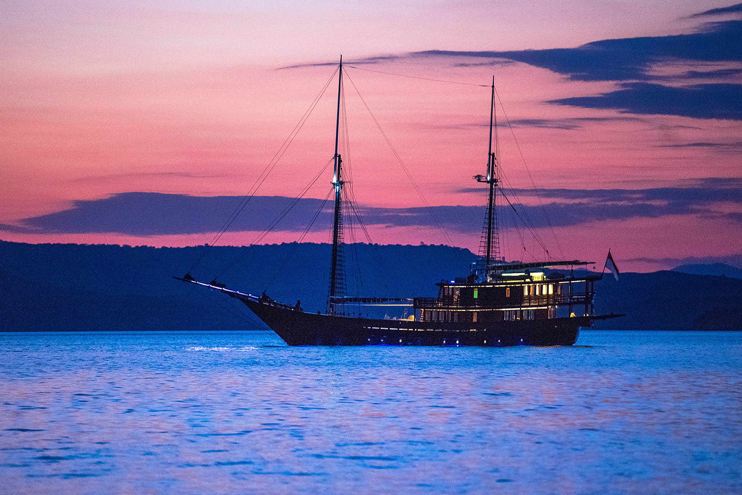 Dunia Baru lit at anchor beneath a violet sky after sunset.