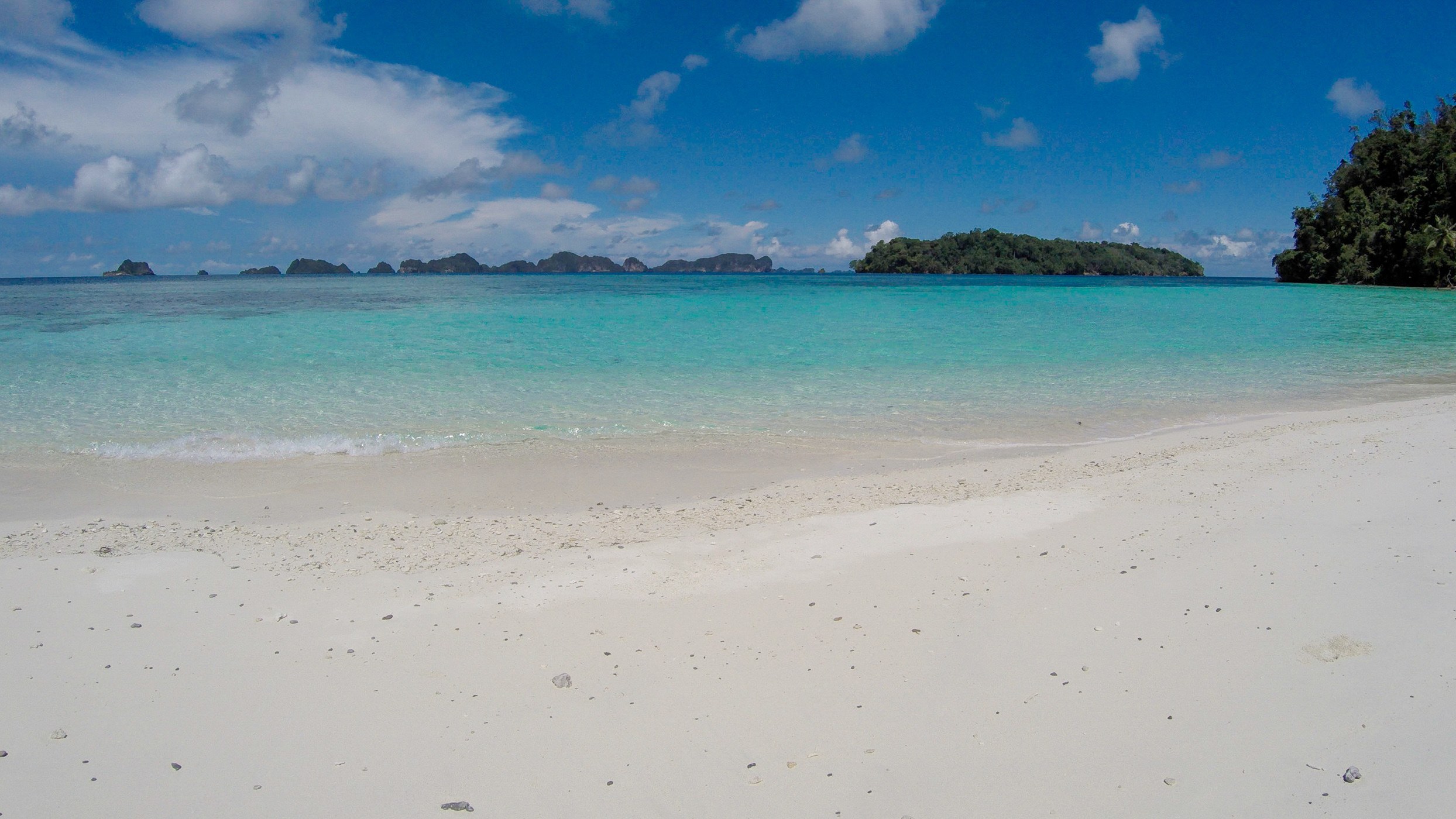 An empty white-sand beach facing small islands across a turquoise lagoon