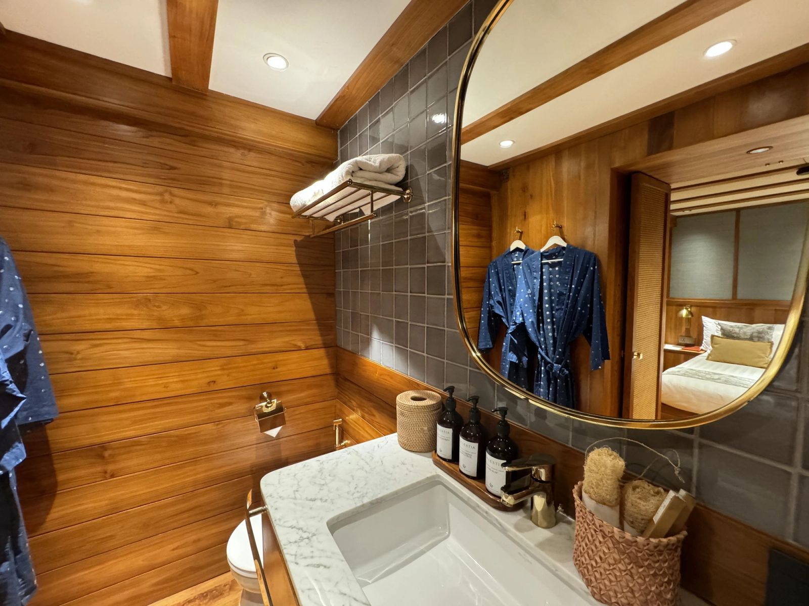 A guest bathroom on Celestia with a round mirror, wood paneling and a vanity.