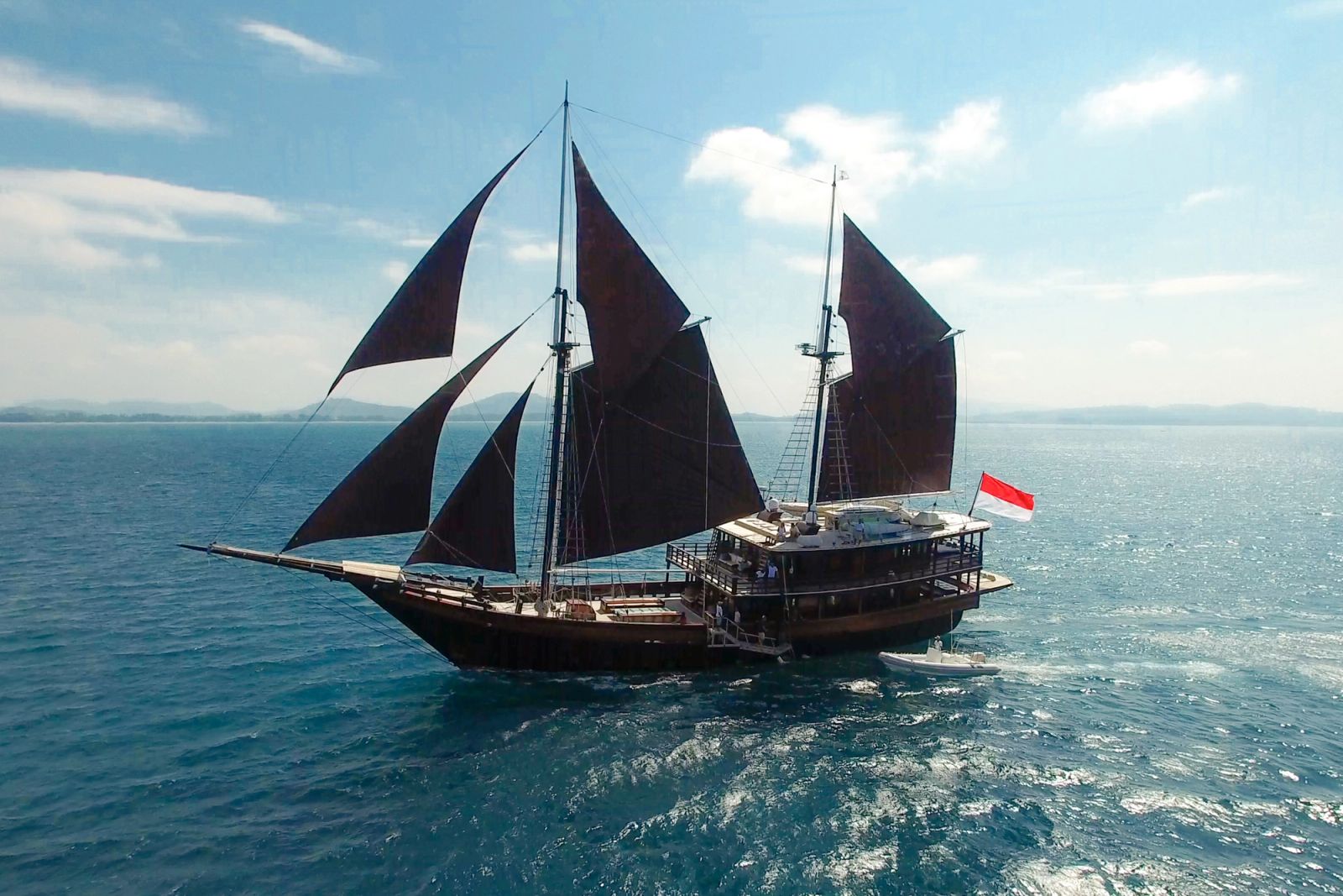 Dunia Baru under dark sails on open water, the Indonesian flag at her stern