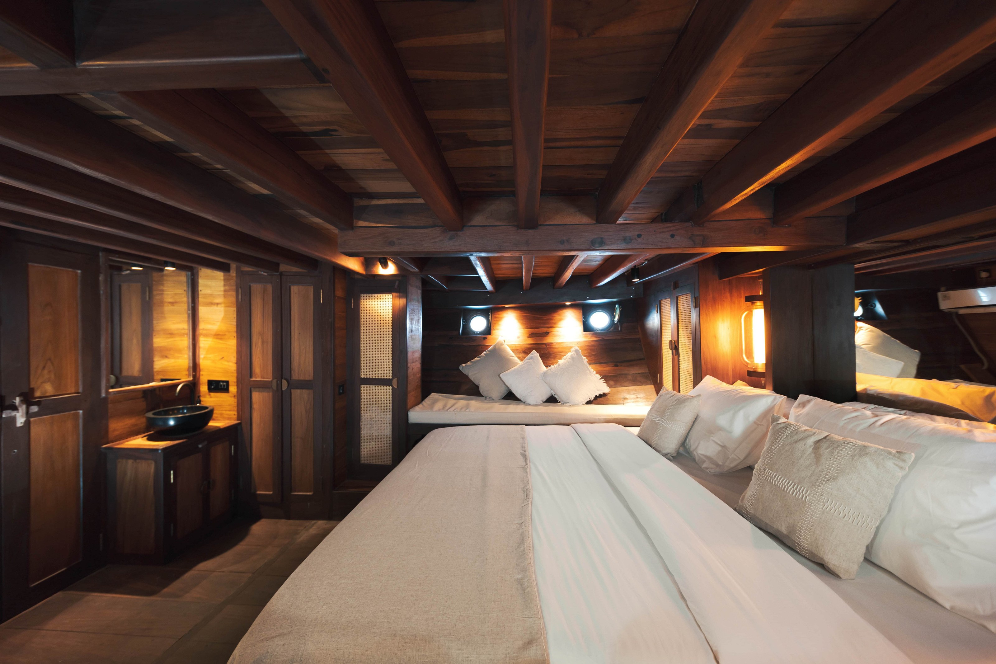 The front cabin on Nataraja, a wide bed lit by warm wall lights.