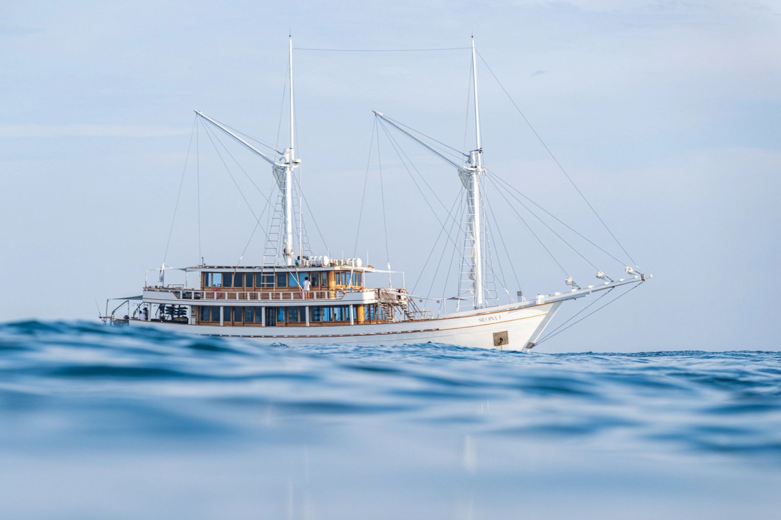 Siloina at anchor on a calm blue sea with her two masts and upper deck.