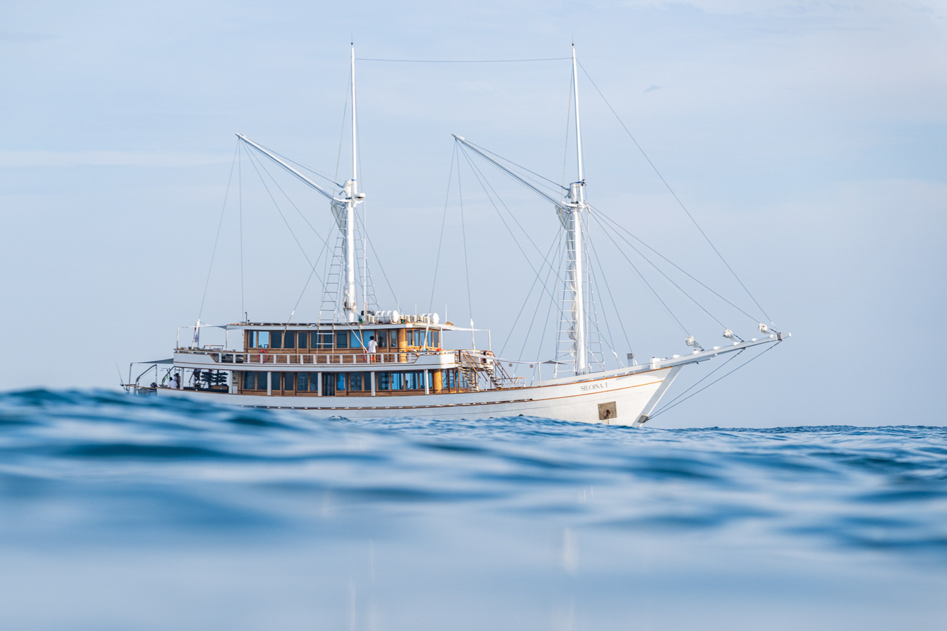 Siloina at anchor on a calm blue sea with her two masts and upper deck.