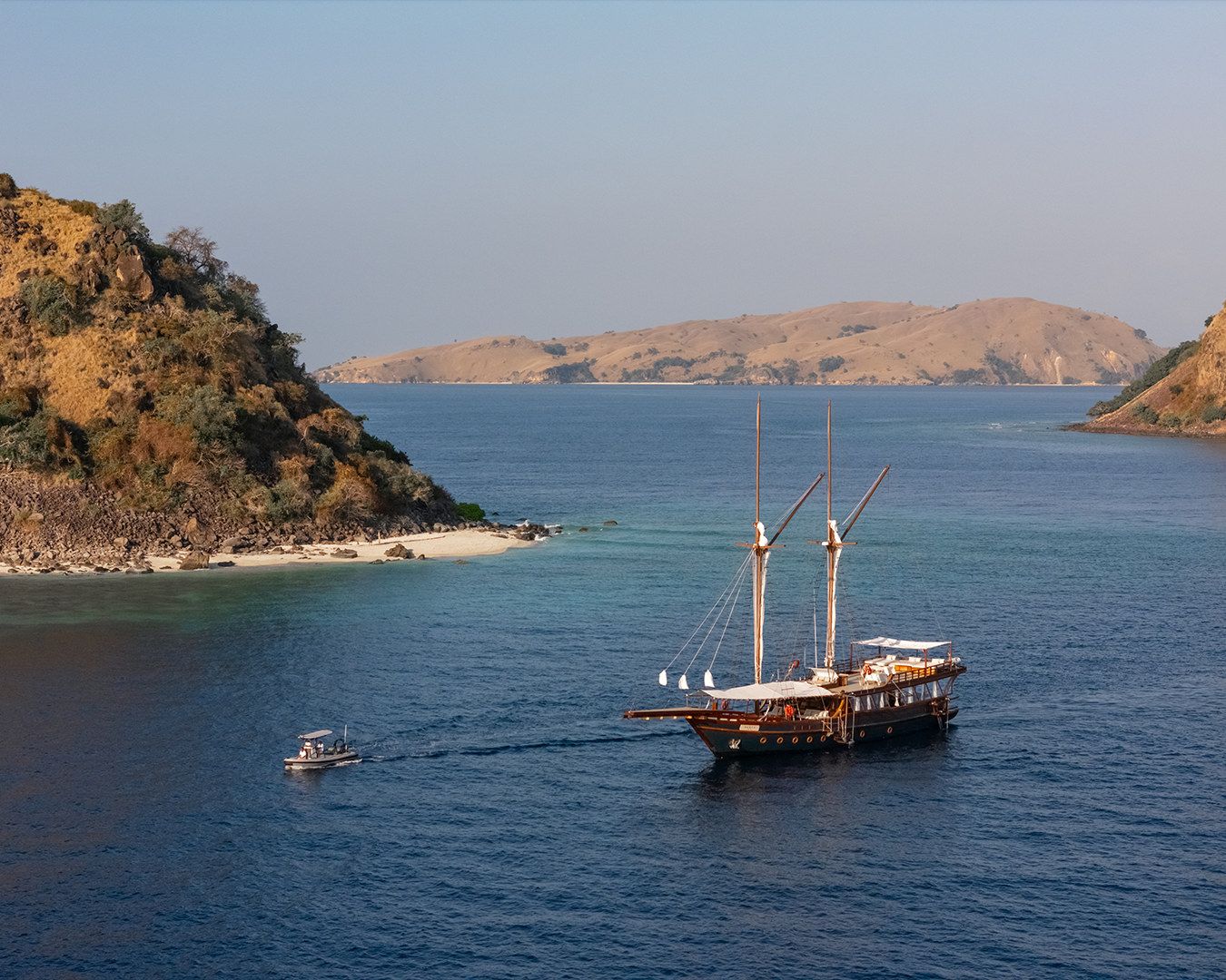 Sanya at anchor beside a rocky headland with her tender alongside.