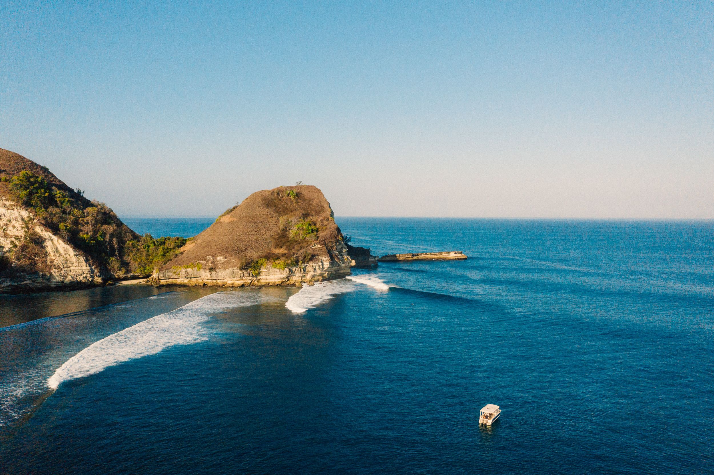 A tender anchored off a headland as waves wrap the point in the Savu Sea