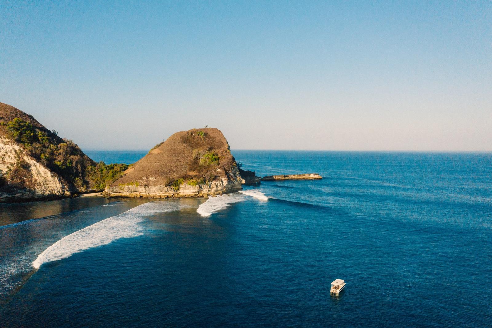 A tender anchored off a headland as waves wrap the point in the Savu Sea