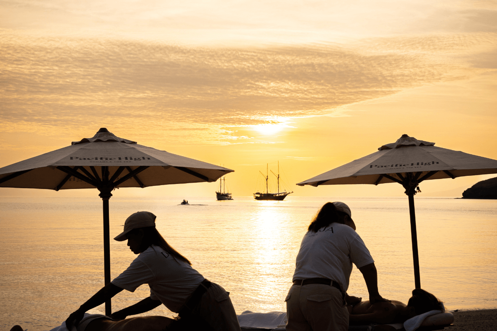 A beach massage under parasols at sunset with phinisis offshore