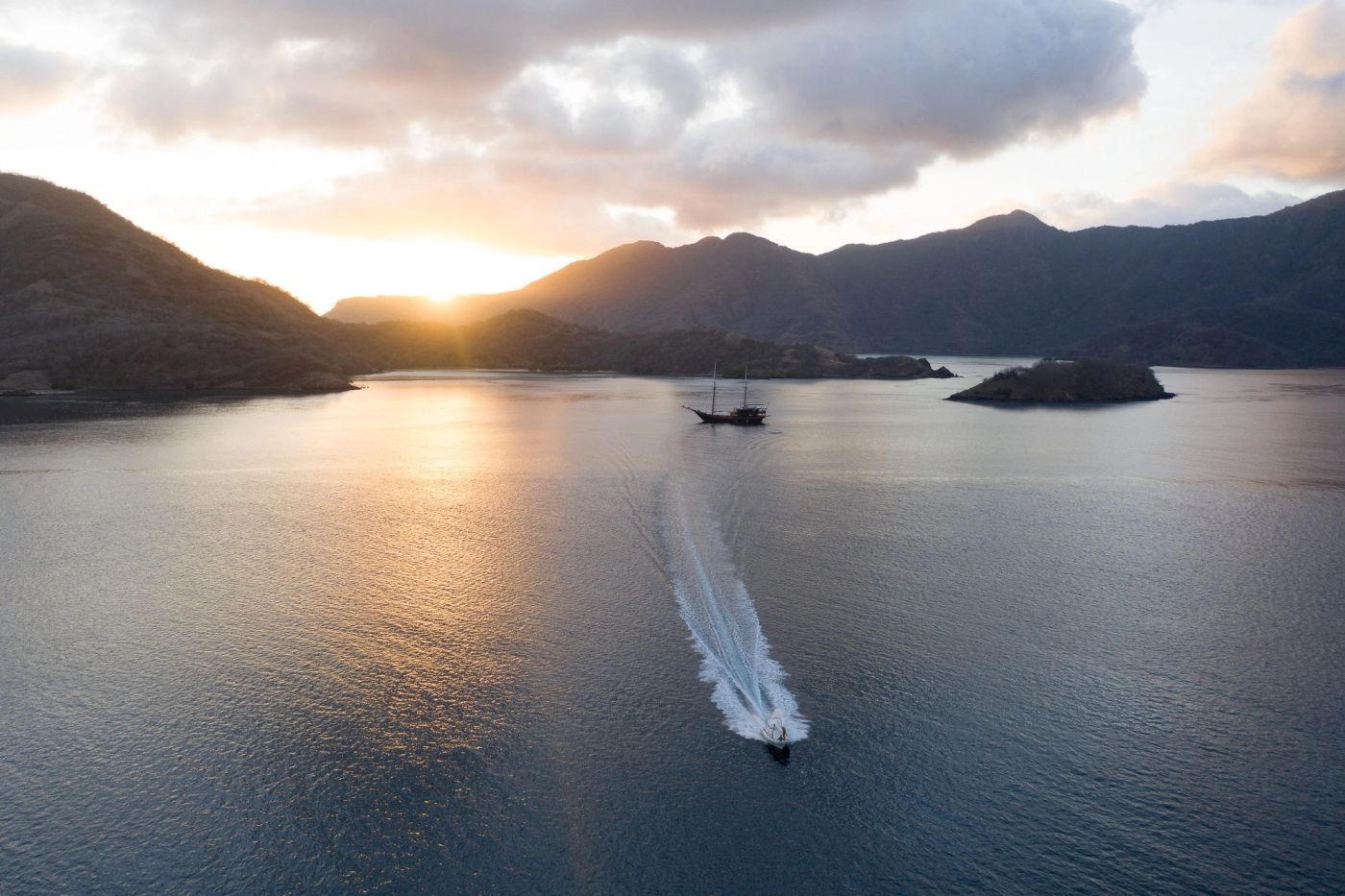 A phinisi at anchor in a golden Komodo bay with a tender running home