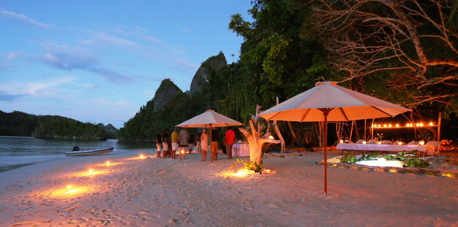 Lanterns and parasols lit on a beach at dusk in Wayag