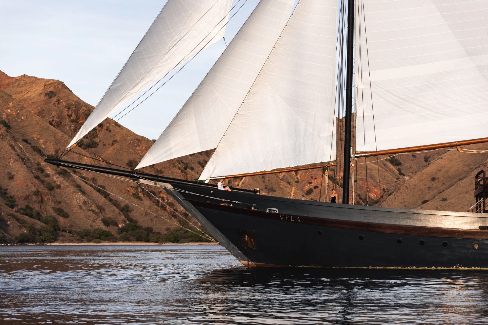 Vela under full sail close along the golden hills of Komodo
