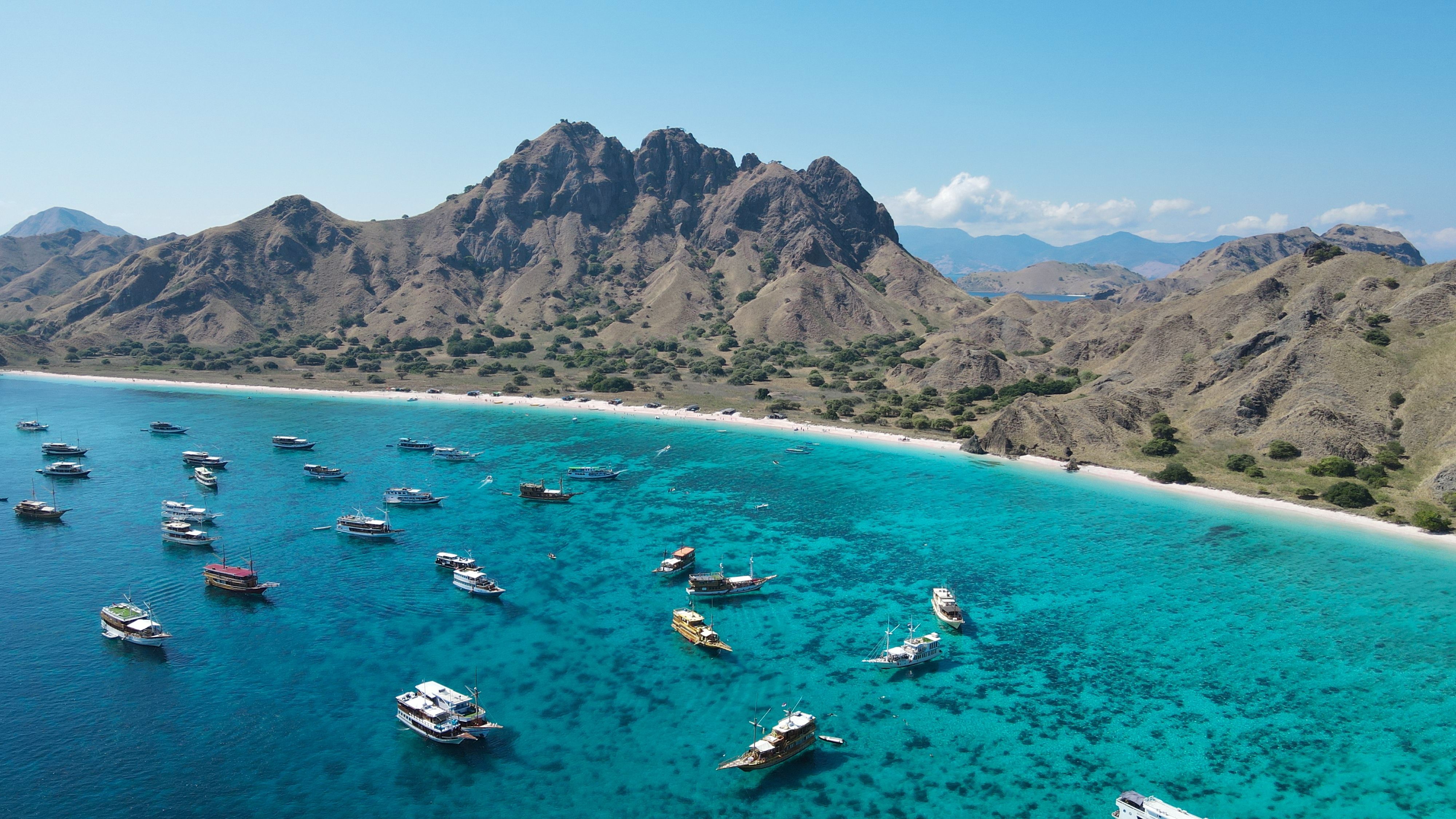 Boats at anchor in a turquoise bay below jagged Komodo hills