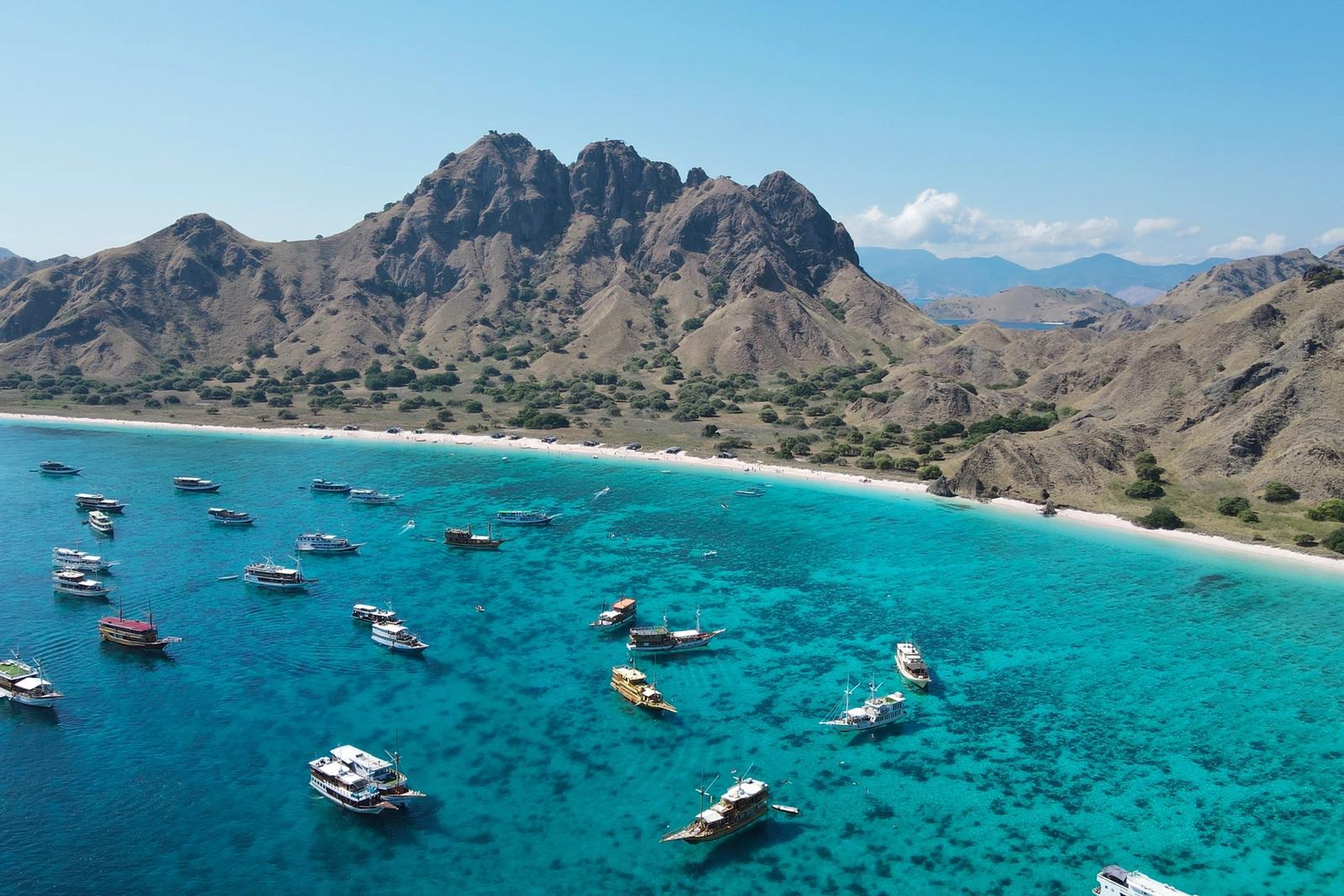 Boats at anchor in a turquoise bay below jagged Komodo hills