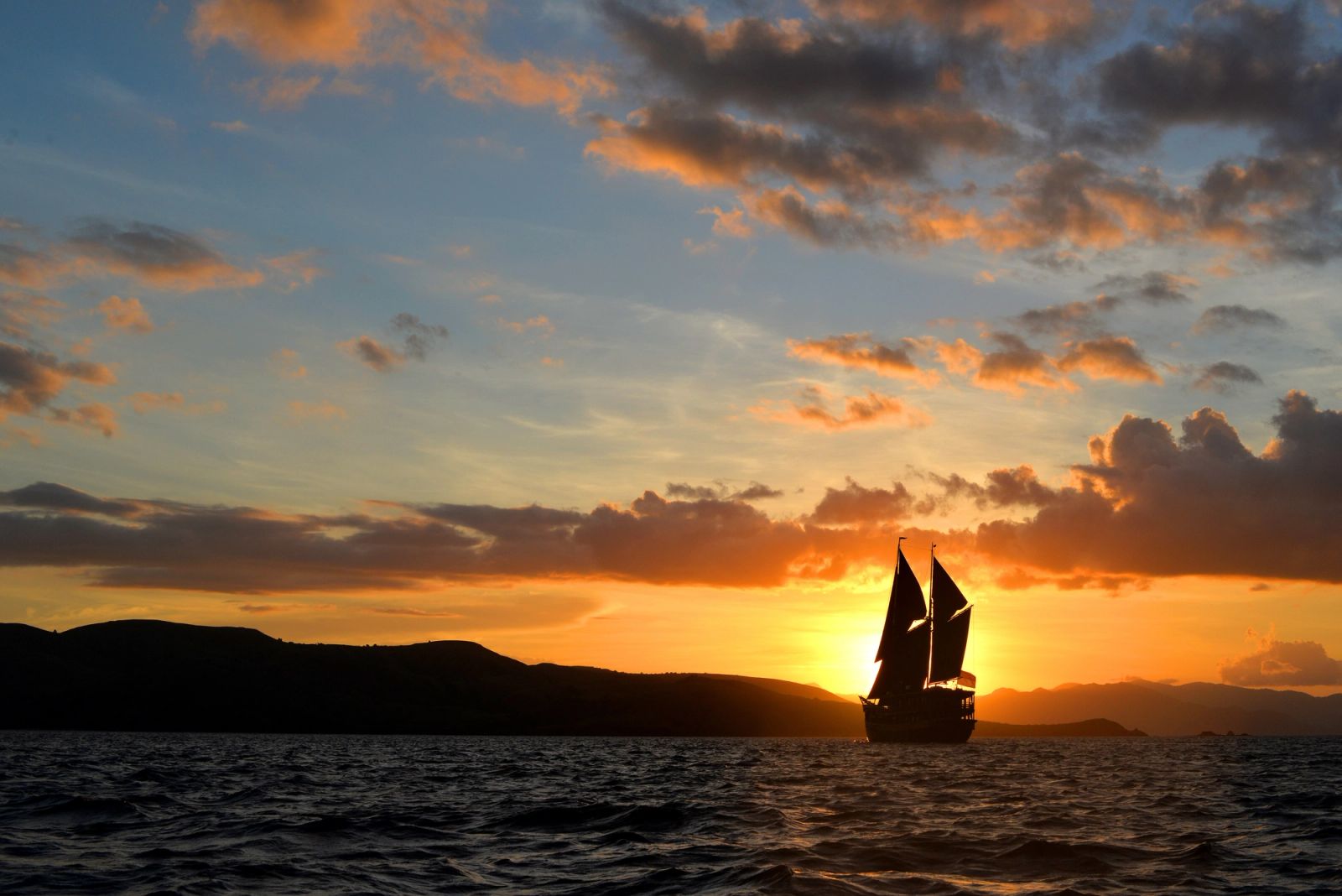 A phinisi silhouetted under sail at sunset