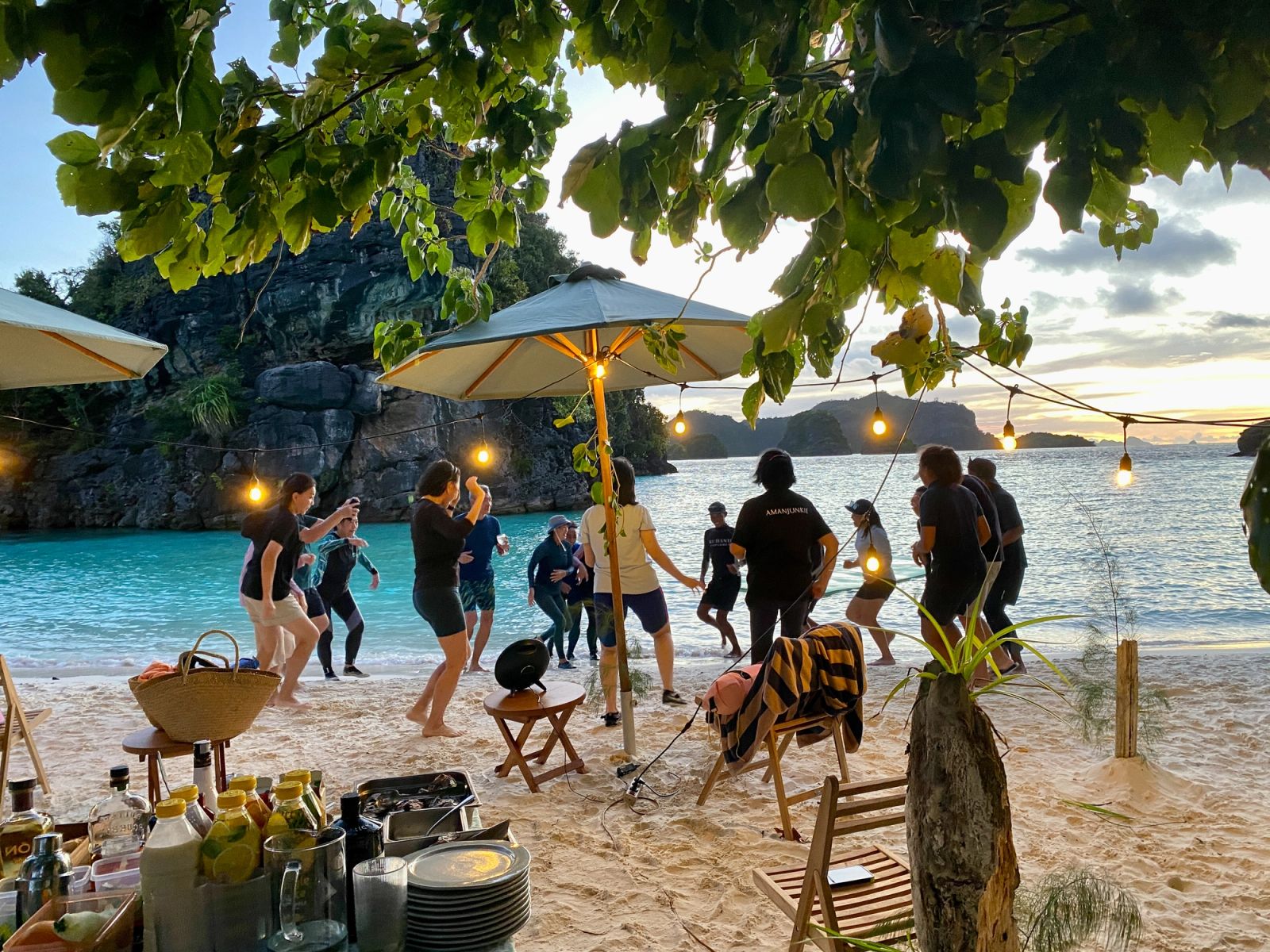 Guests gathered around a beach dinner under lanterns at dusk
