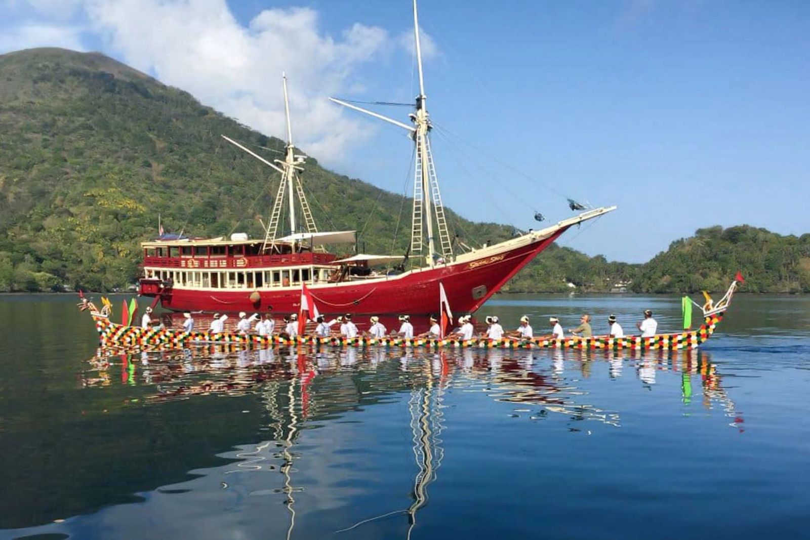A traditional canoe crew rowing past The Seven Seas at anchor