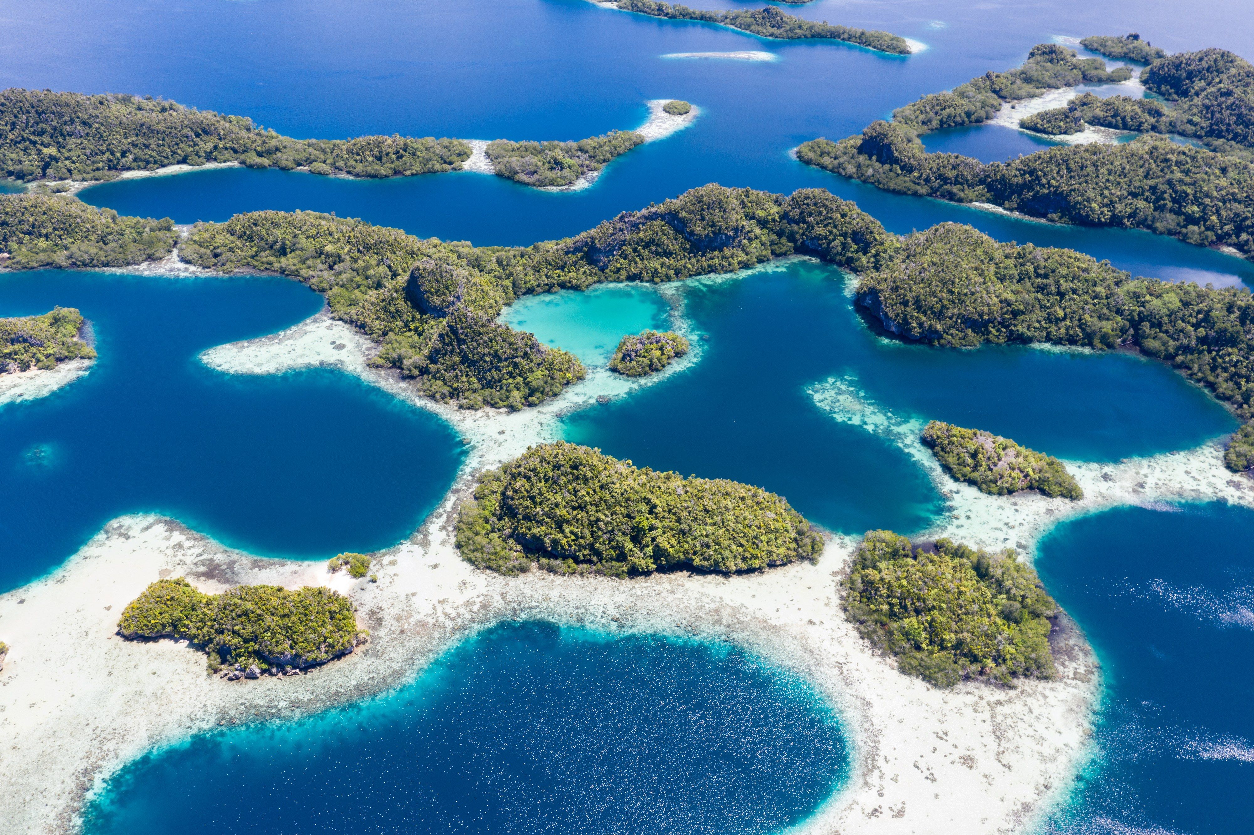 Remote limestone islands ringed by coral reefs and blue lagoons in Raja Ampat, seen from the air