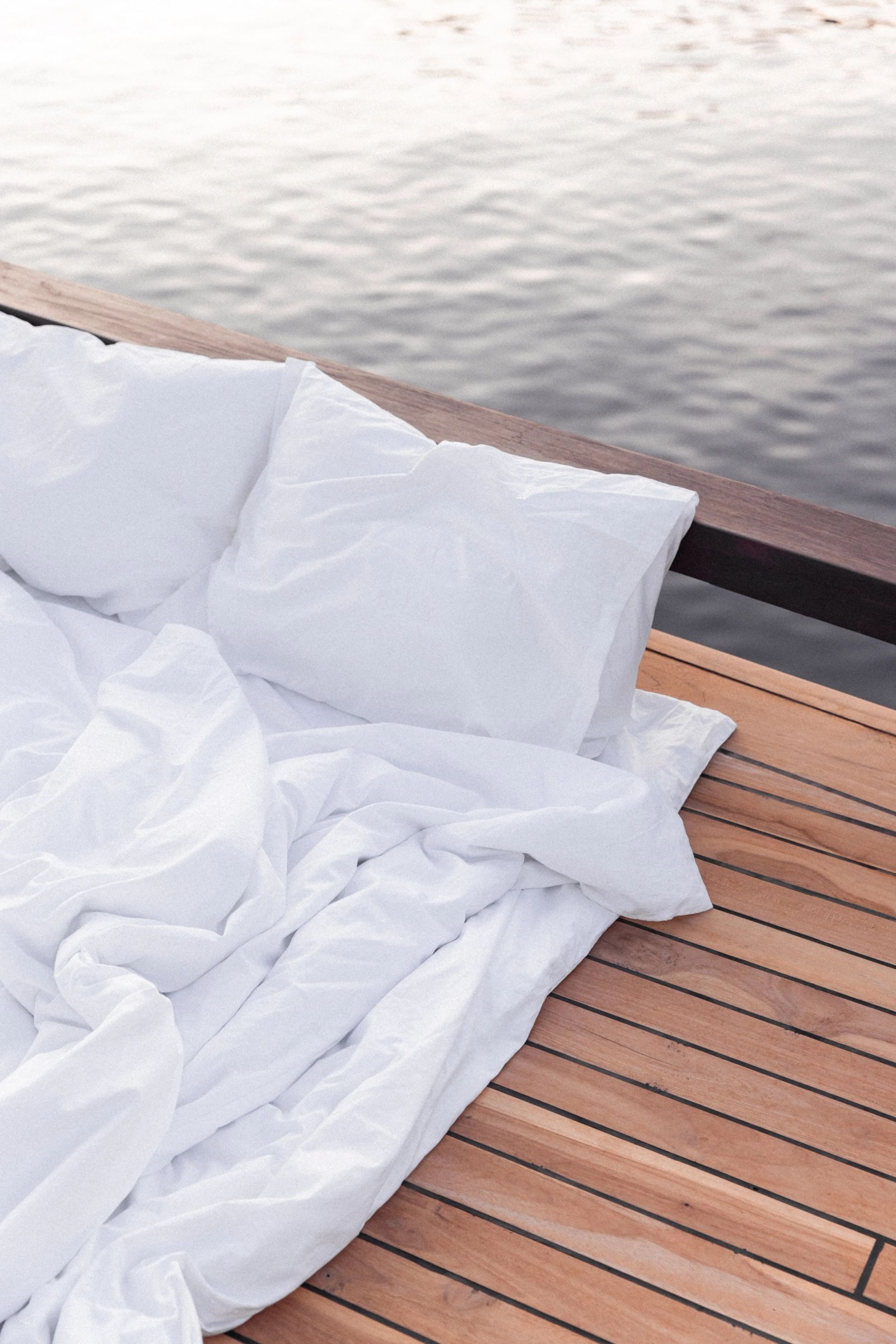 A bed made up with white linens on Vela's teak aft deck at dawn