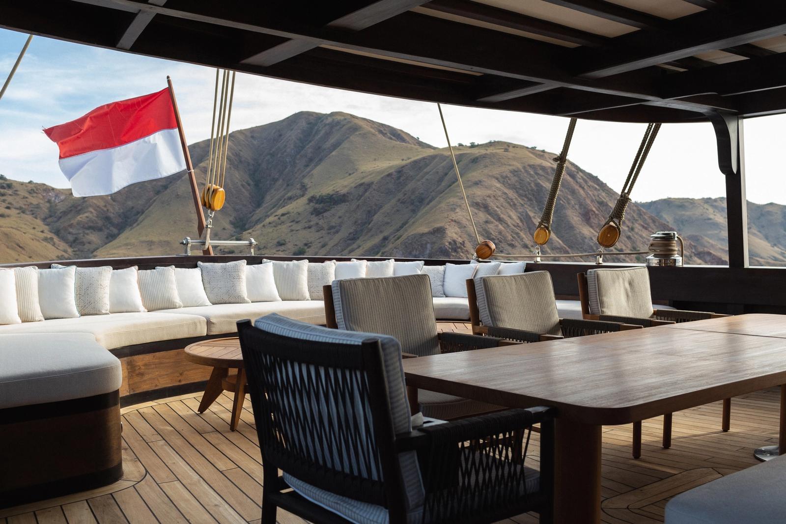 A shaded deck lounge and dining table with the Indonesian flag and Komodo hills