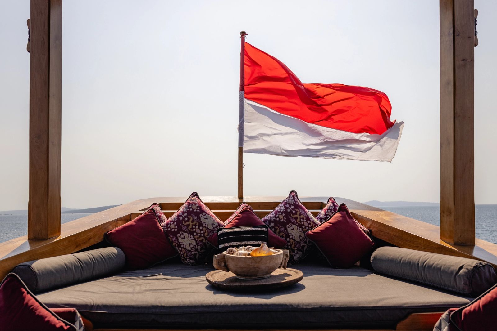 Silolona's aft deck lounge with red cushions and the Indonesian flag