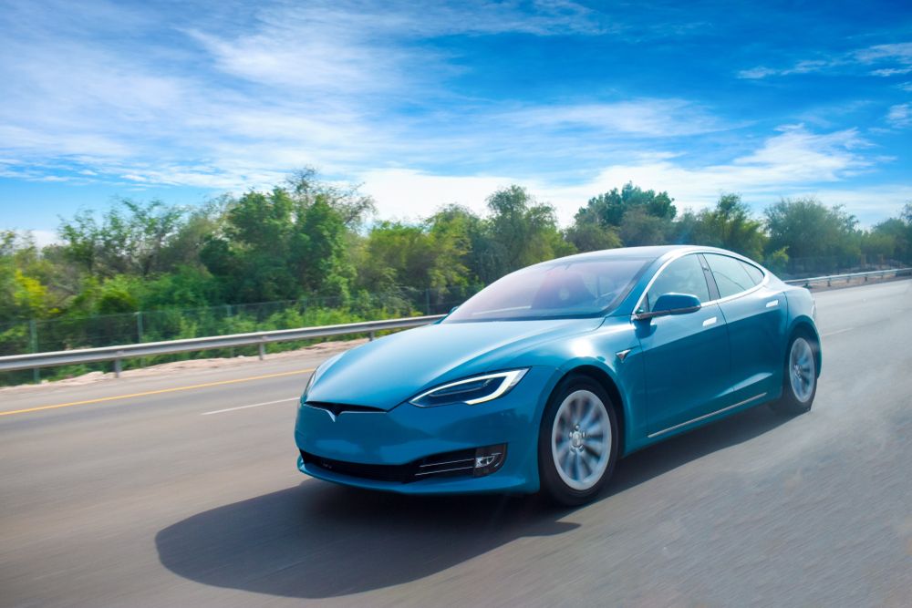 A blue Tesla Model S driving on a highway under a clear blue sky, illustrating a Virginia Lemon Law EV claim for defective electric vehicles.