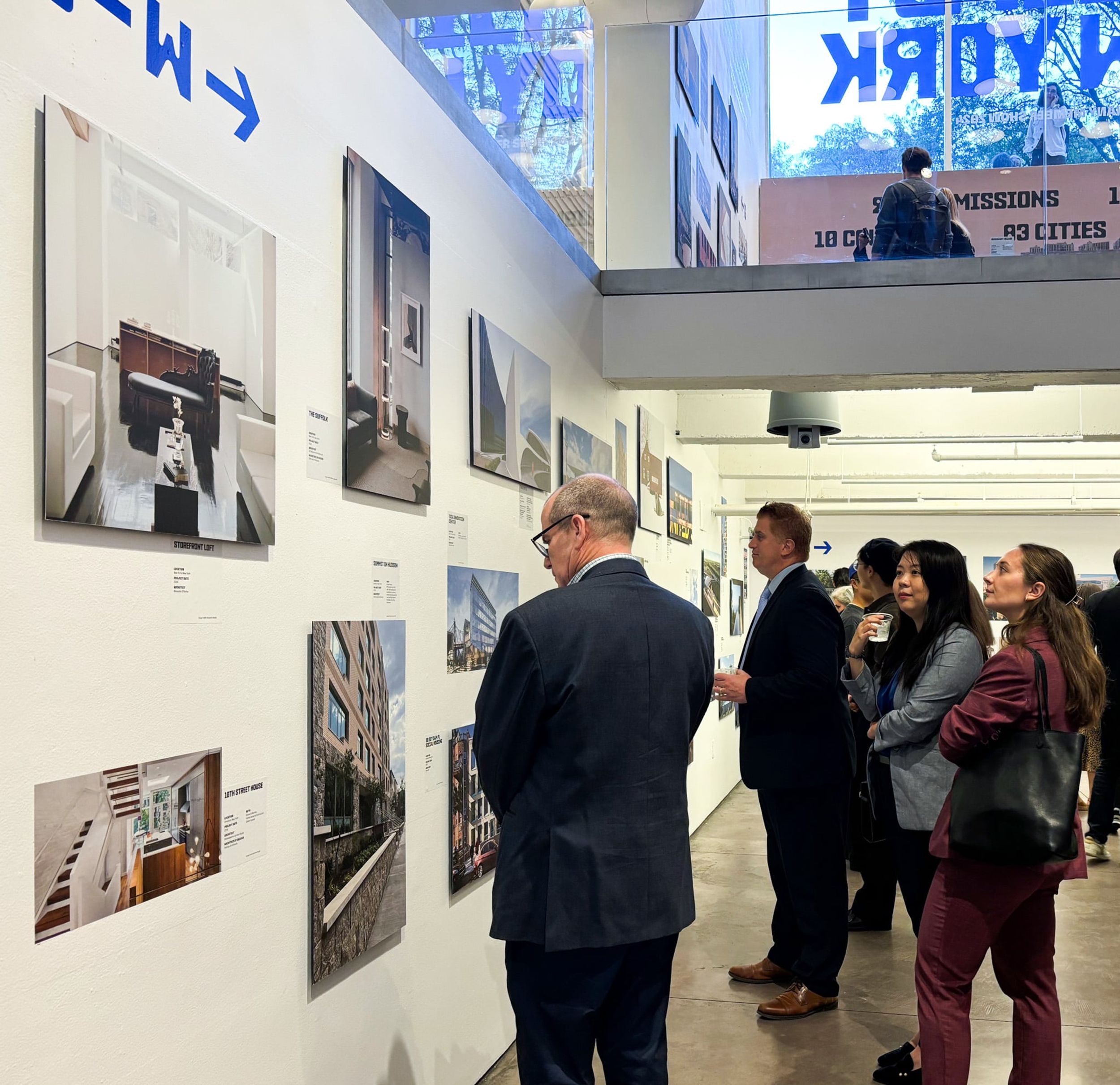 View of gallery wall with photo of 10th Street House by SGS and onlookers