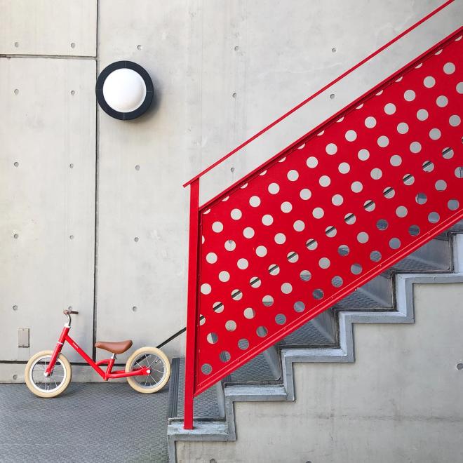 A red children's balance bike at the base of concrete stairs
