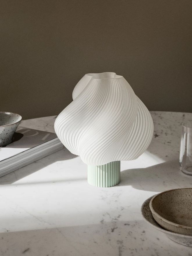 Soft Serve table lamp glowing softly on a table next to a glass of water