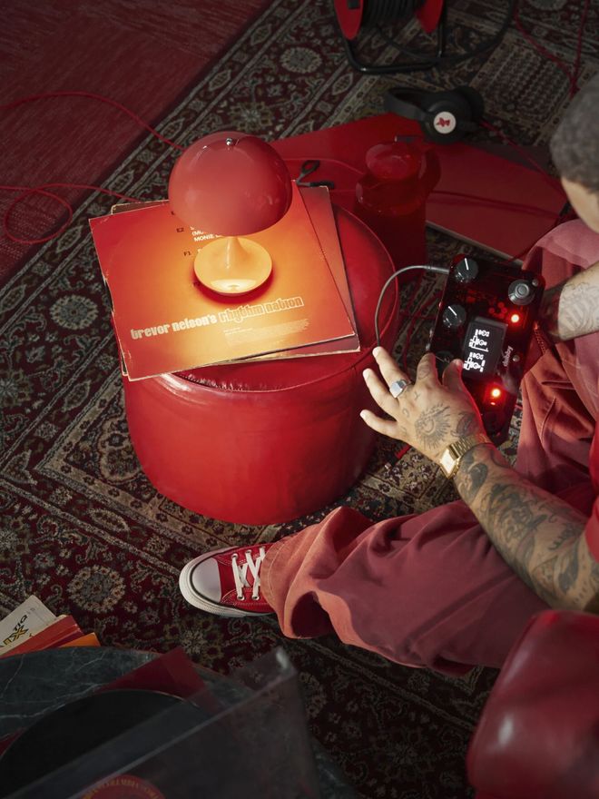 Coral Panthella Portable lamp on top of vinyl records on a red leather pouf, next to a person adjusting an electronic instrument.