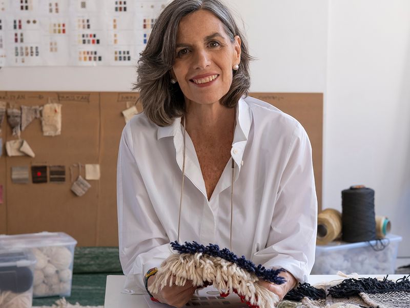 Designer Nani Marquina in front of a work desk, holding textile samples and smiling at the camera