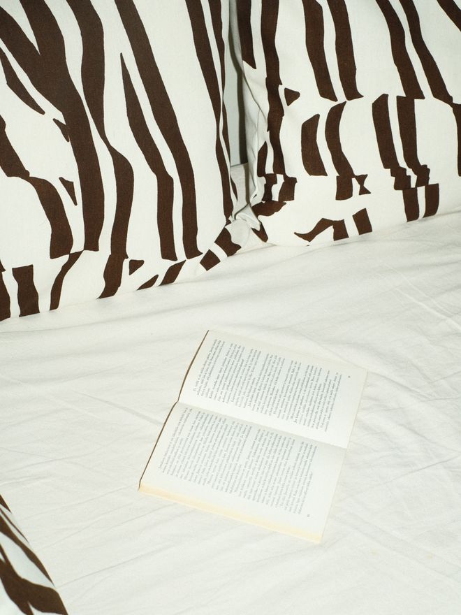 An open book on a bed next to a black-and-white striped cushion