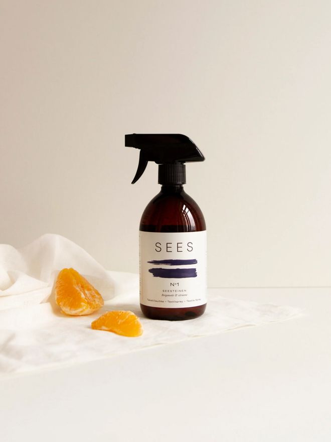 A bottle of SEES Company textile spray and orange slices on the edge of a light textile