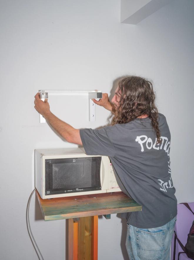 Fredrik Paulsen person mounts a white wall shelf on the wall above a microwave.