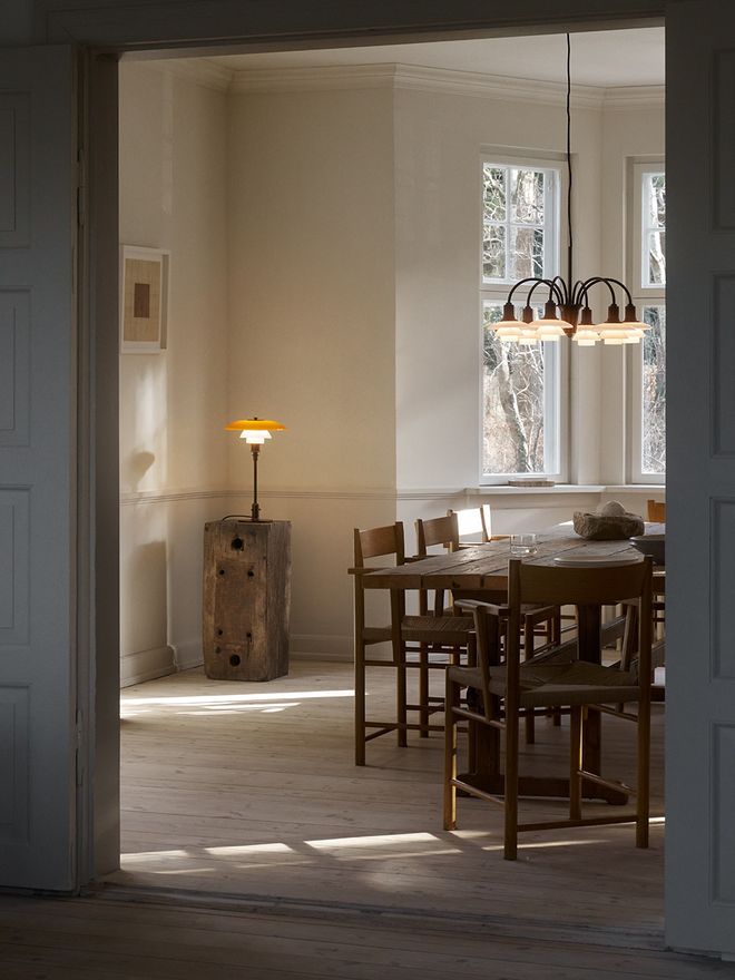 Louis Poulsen PH 3/2 Table Lamp Centenary Edition in aged brass with amber upper shade and white opal glass lower shades, displayed on a weathered wooden block in a bright Scandinavian interior