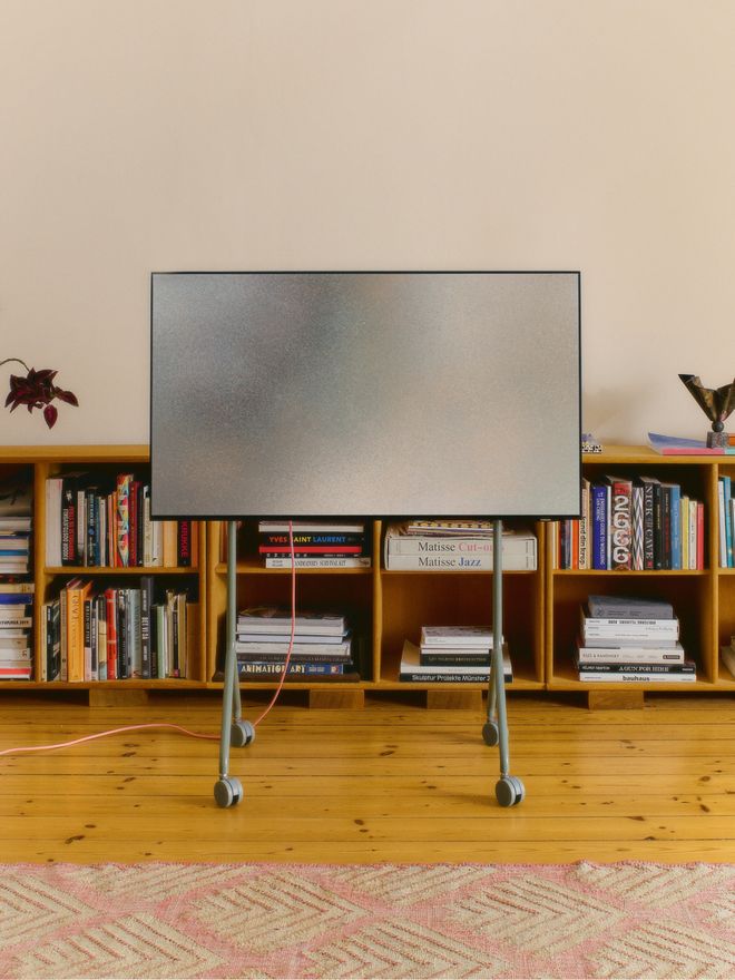 A television on a slim TV stand in a living room, with a low bookshelf in the background.